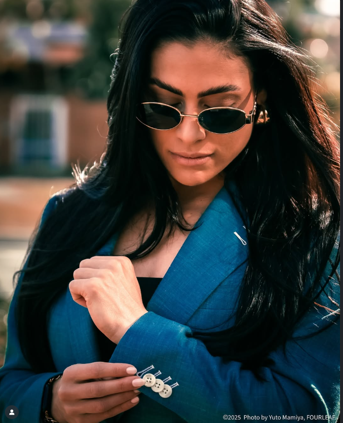 Woman wearing sunglasses and a blue coat and suit, holding a small object.
