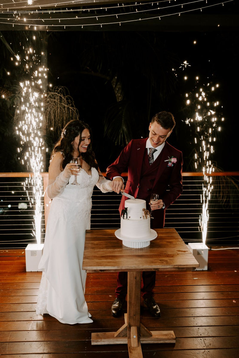 Couple cutting a wedding cake with fireworks in the background